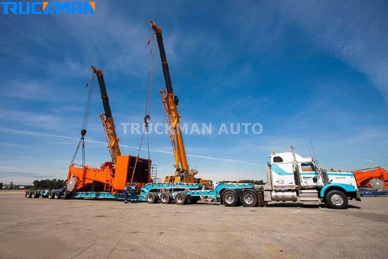Dos grúas móviles elevando equipos pesados sobre un semirremolque de plataforma baja