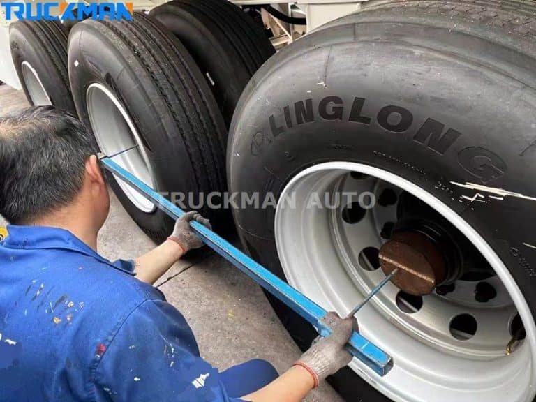 Un técnico de mantenimiento está comprobando y manteniendo la presión de los neumáticos de un semirremolque de plataforma baja, utilizando herramientas para asegurarse de que los tornillos de los neumáticos están apretados