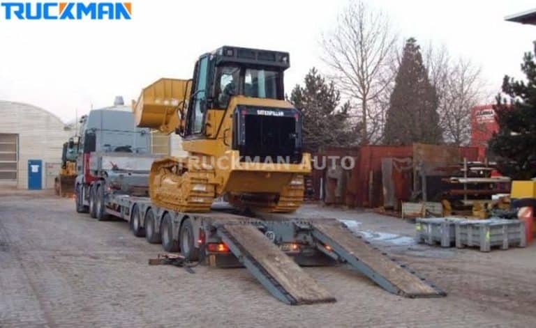 Maquinaria de construcción Caterpillar siendo cargada en un semirremolque de plataforma baja con rampas metálicas