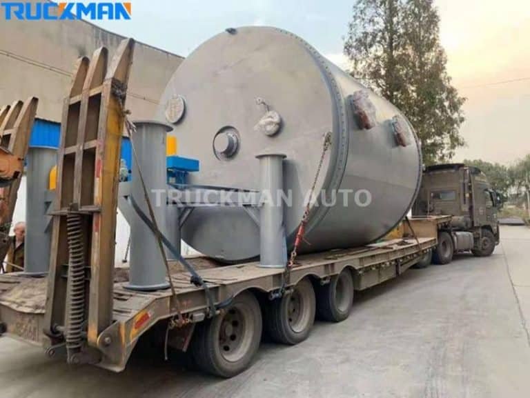 Semirremolque de plataforma baja para cargas pesadas que transporta un tanque de almacenamiento industrial sobredimensionado.