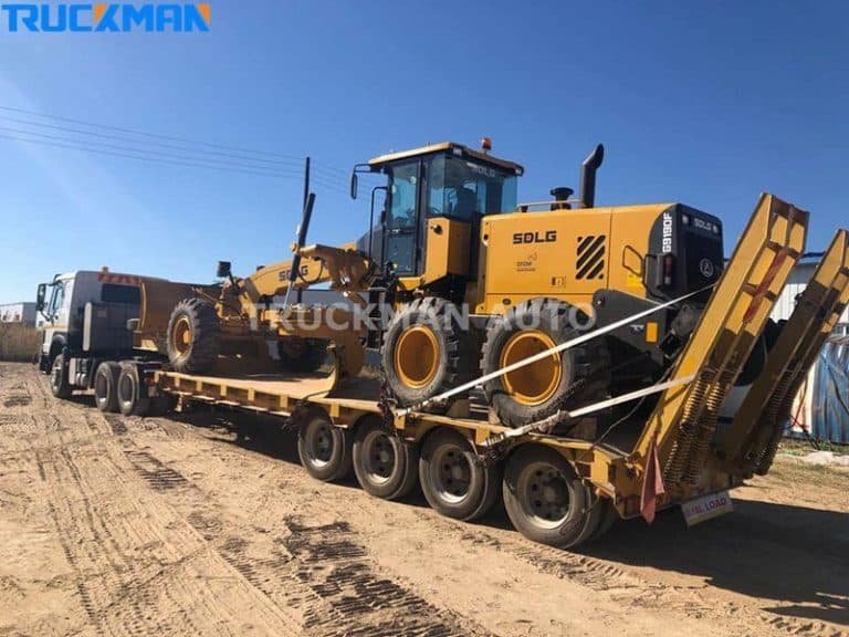 Gran niveladora de construcción asegurada en un semirremolque de plataforma baja de varios ejes en un terreno de tierra
