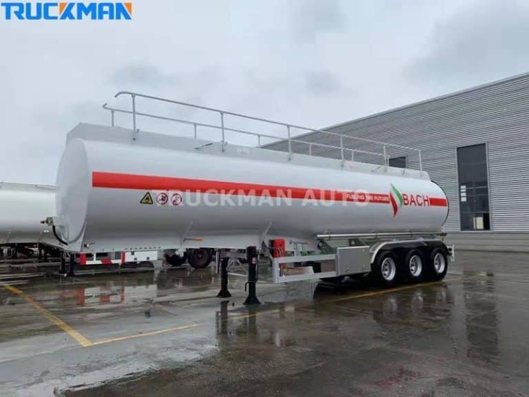 Camión cisterna de combustible blanco modernizado con el logotipo de Mercancías Peligrosas, aparcado sobre la superficie mojada de un polígono industrial.