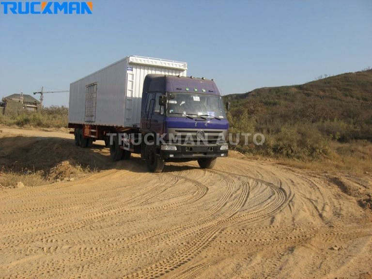 Camión con remolque de furgoneta circulando por un camino de tierra, transportando electrodomésticos y materiales de construcción-Camionero Automóvil
